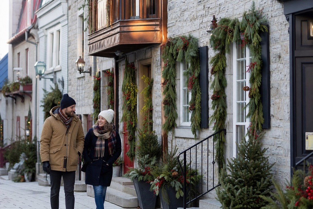 Couple walking past decorated stone houses in the Petit Champlain district of Quebec City at Christmas