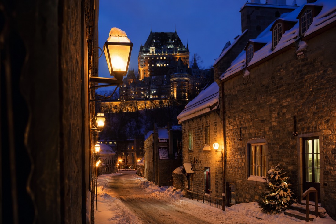 Lantern-lit night street in Old Quebec in winter with snow on cobblestones and old stone walls