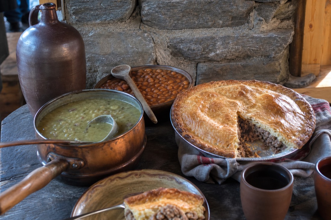 Rustic Quebec table set with tourtière, baked beans, pea soup and a jug of maple syrup