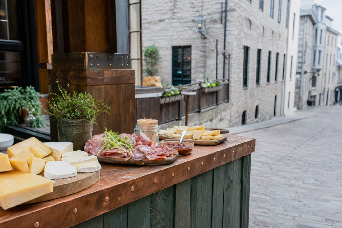 Small group tasting cheese and charcuterie at a market counter on a cobbled Old Quebec street