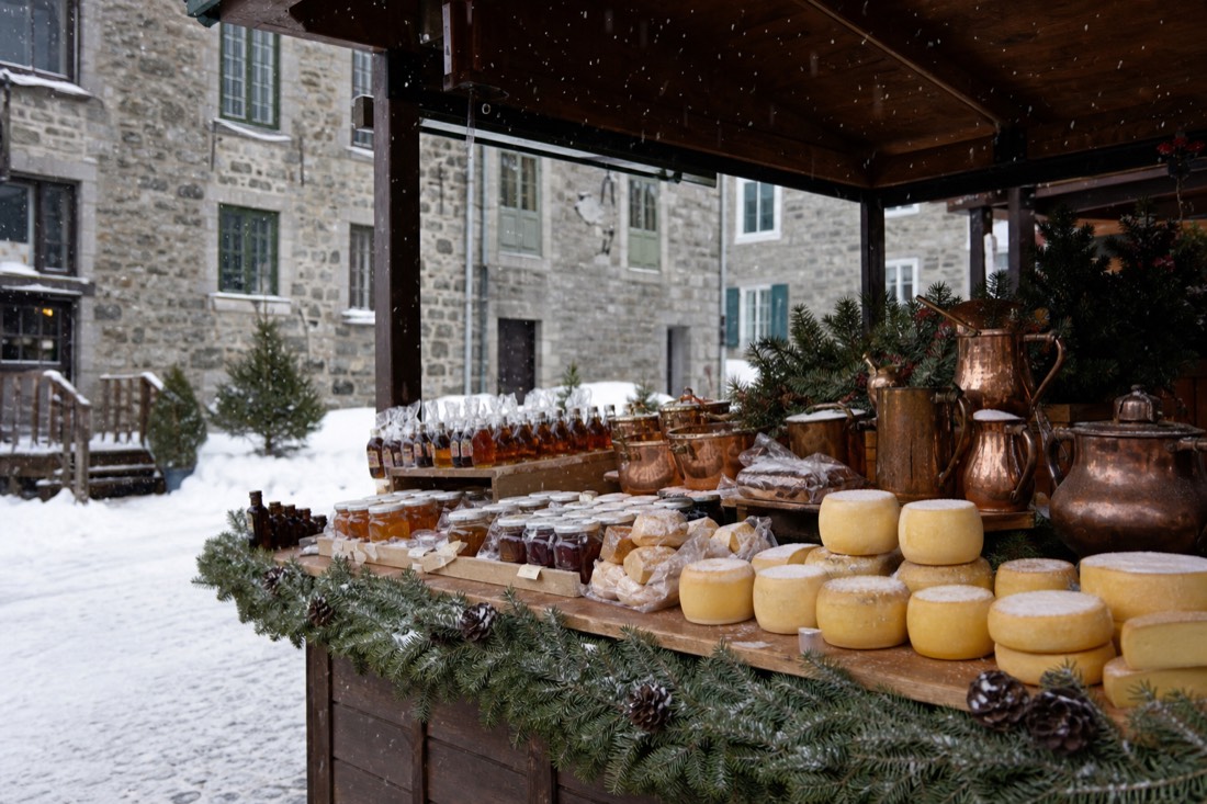 Winter market stall in Old Quebec selling maple products and cheese under falling snow