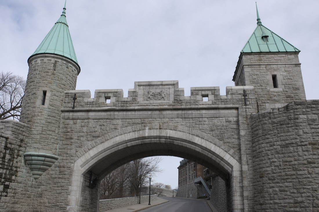 Stone archway of a Quebec City fortification gate with turrets, seen from the street below