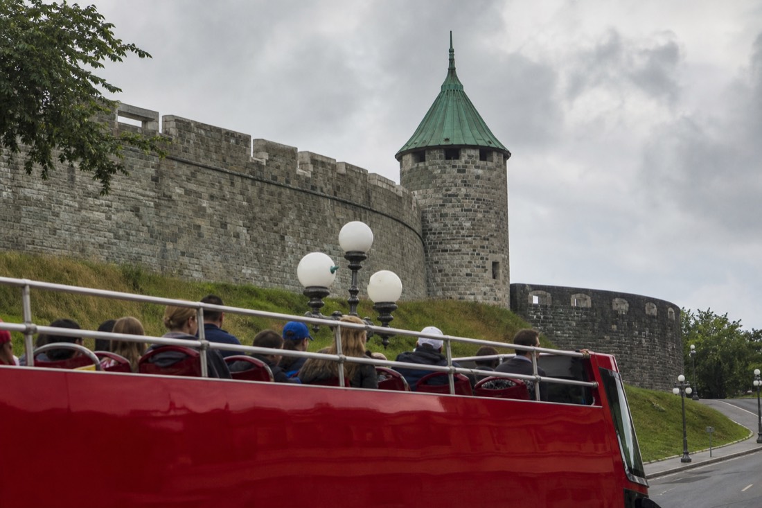 Double-decker sightseeing bus passing the old city walls of Quebec with families on the open top deck