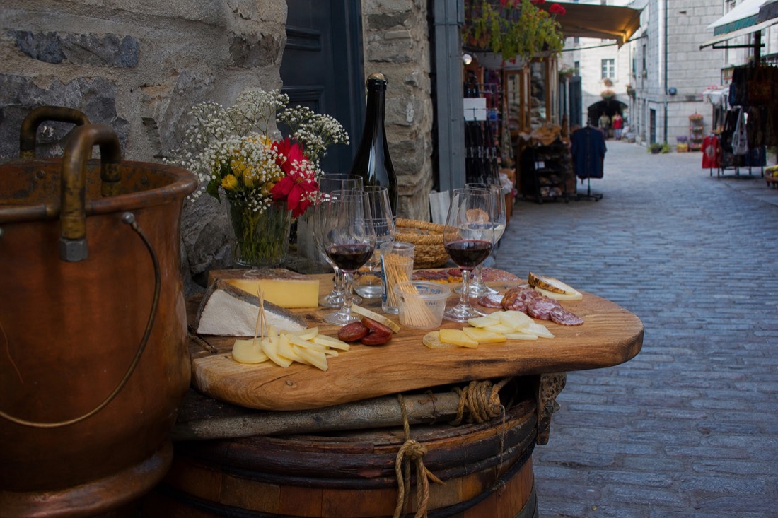 Small group tasting cheese and charcuterie at a market stall on a cobbled Old Quebec street
