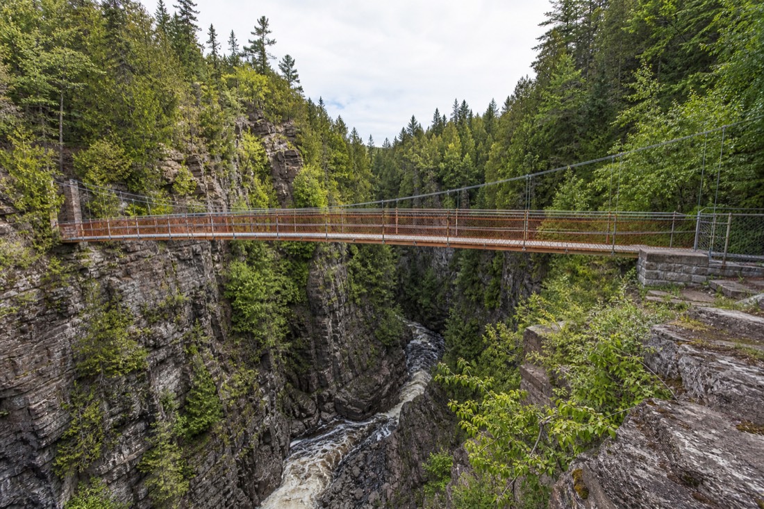 Comparison view of a suspension footbridge over the narrow Canyon Sainte-Anne gorge with rapids below