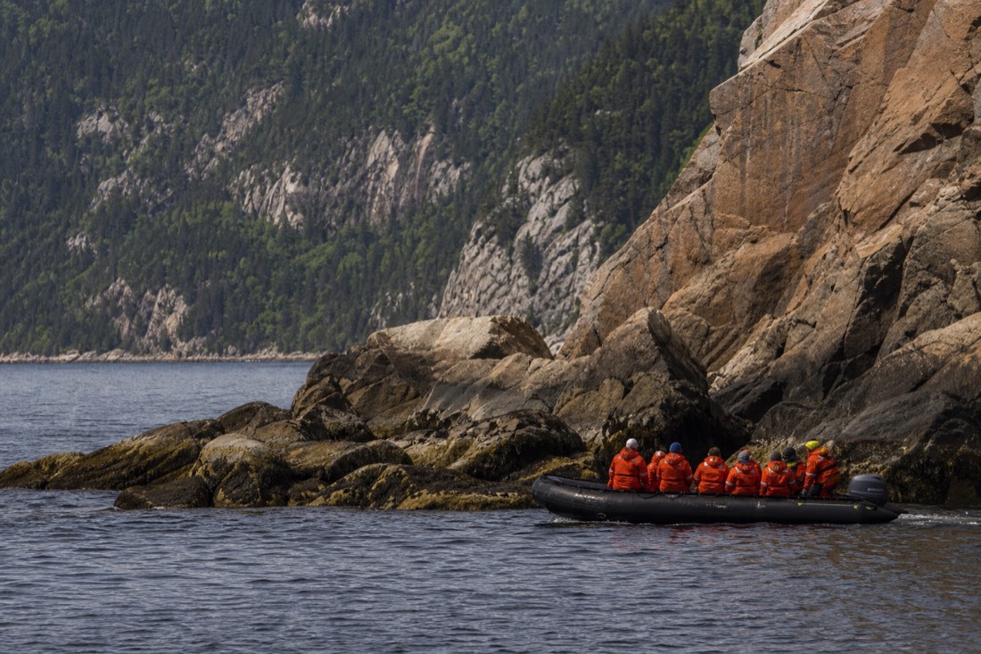 Zodiac boat carrying passengers in orange survival suits on the St. Lawrence near Tadoussac beyond Charlevoix