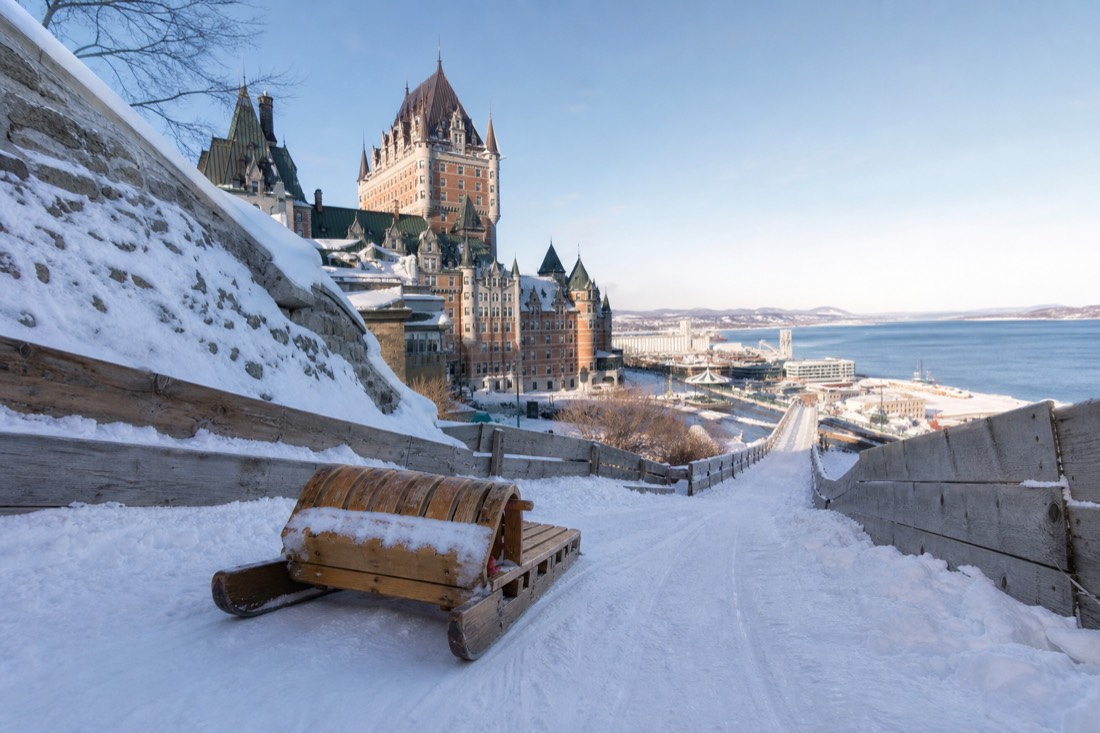 Wooden toboggan sled speeding down the Dufferin Terrace slide in winter with the Château Frontenac behind