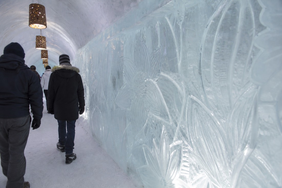 Visitors on a day tour walking past sculpted ice walls inside the Hôtel de Glace at Valcartier