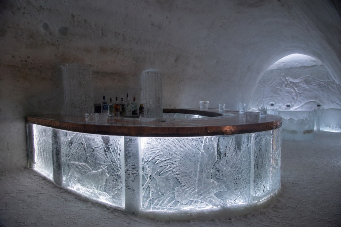 Ice bar with backlit sculpted counter and ice glasses inside the Hôtel de Glace at Valcartier