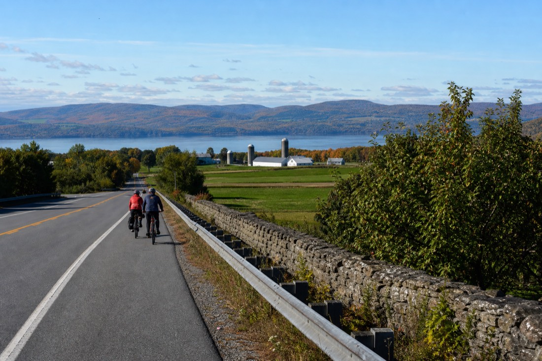 Cyclists on e-bikes riding the shoulder of Route 368 past farmland on Île d'Orléans