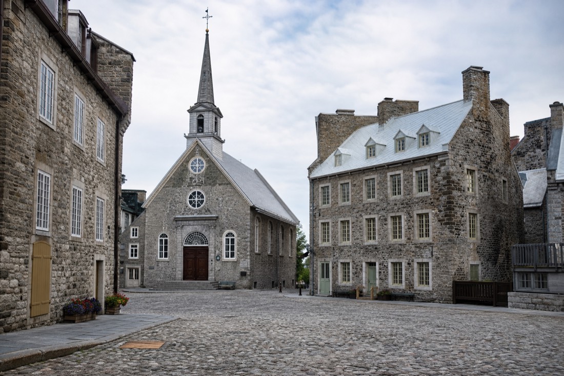 Visitors walking a short route across Place Royale past the church and stone houses in Lower Town Quebec City