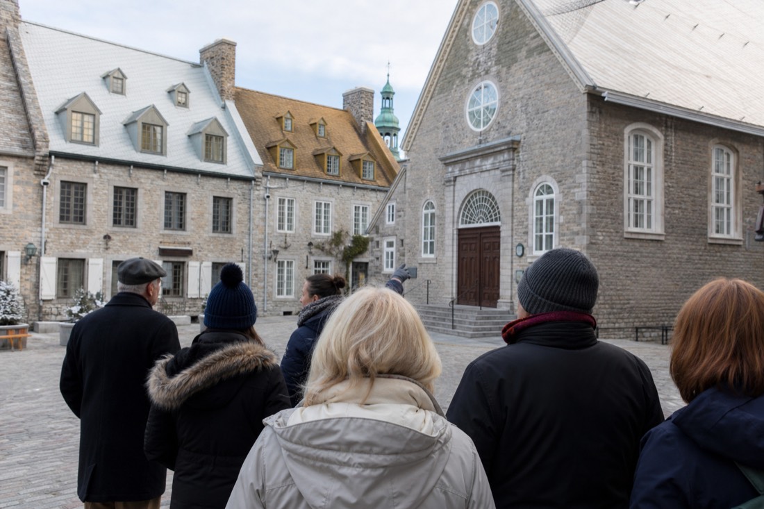 Guide leading a small walking tour group into Place Royale beside the stone church in Old Quebec