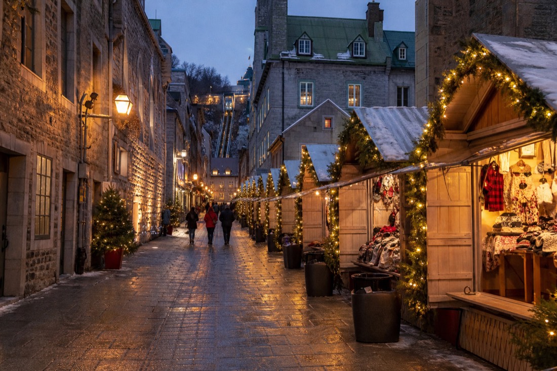 Visitors walking between lit Christmas market kiosks on rue Sainte-Anne in Old Quebec after dark