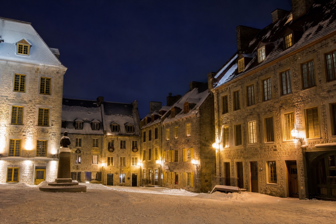 Quiet snow-covered Place Royale at night with warm light from the stone buildings of Old Quebec