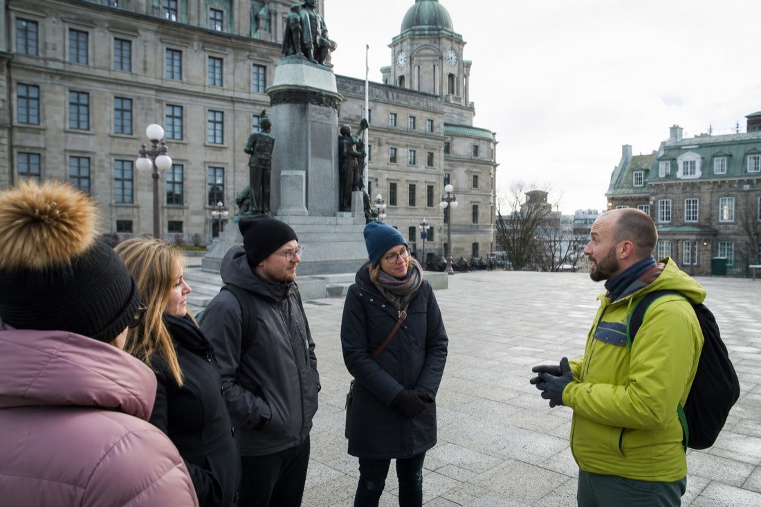 Small group of travellers listening to a guide near Place d'Armes on a free walking tour of Quebec City