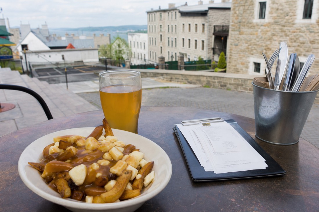 A bistro table in Quebec City set with poutine, a glass of local cider and a printed bill
