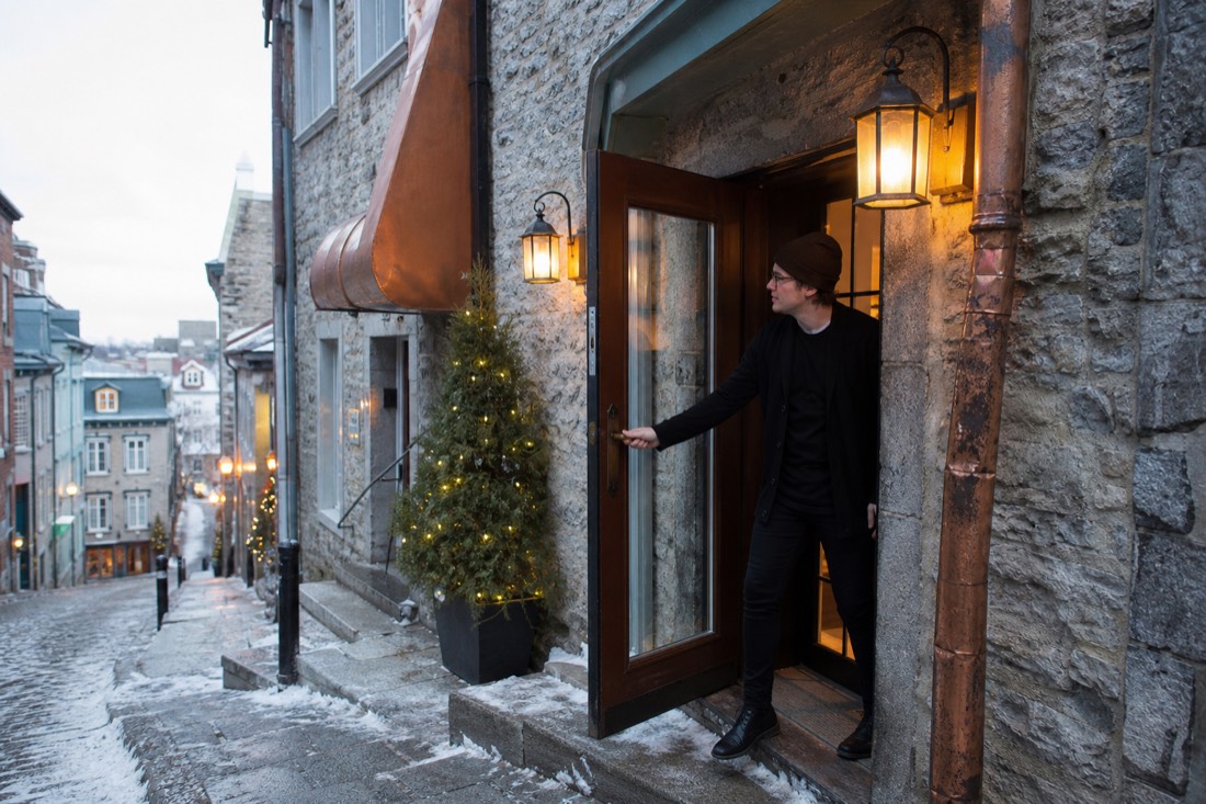 A host greeting guests at the door of a small restaurant in Old Quebec on a winter evening