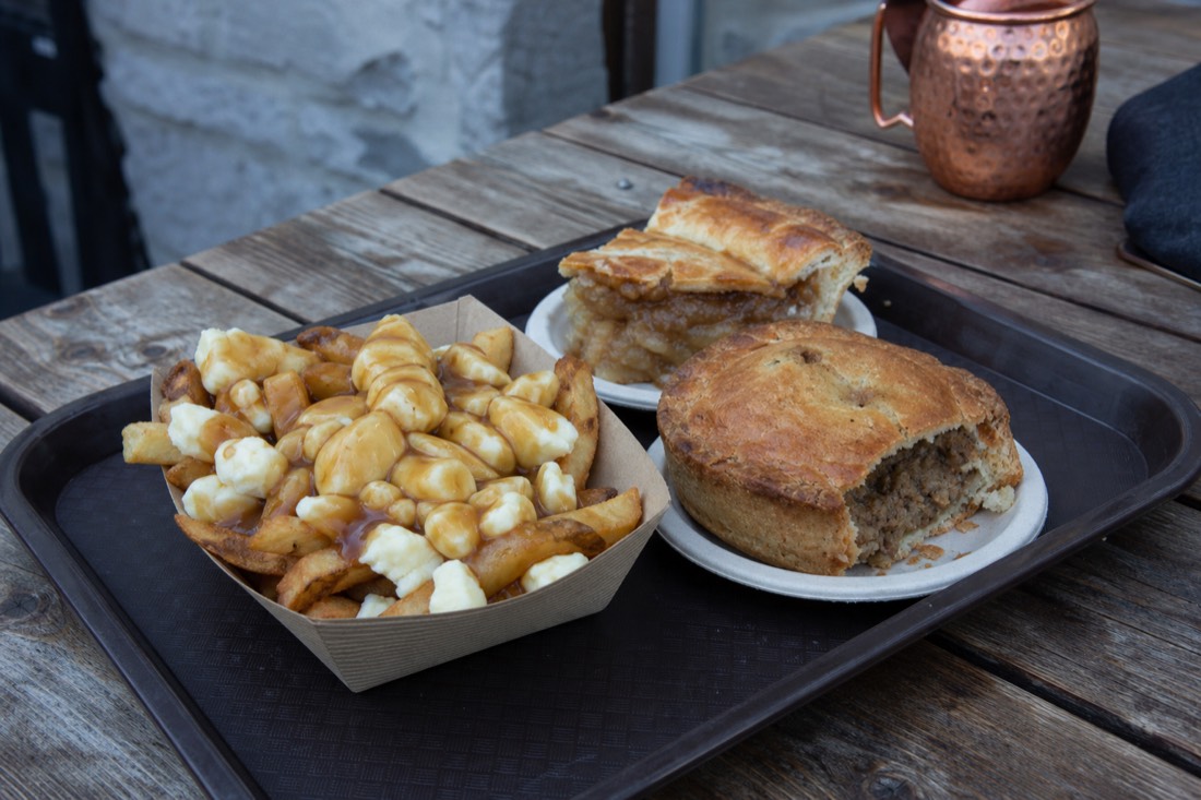A tray of poutine, tourtière and maple pie on a wooden table at a Quebec City snack bar