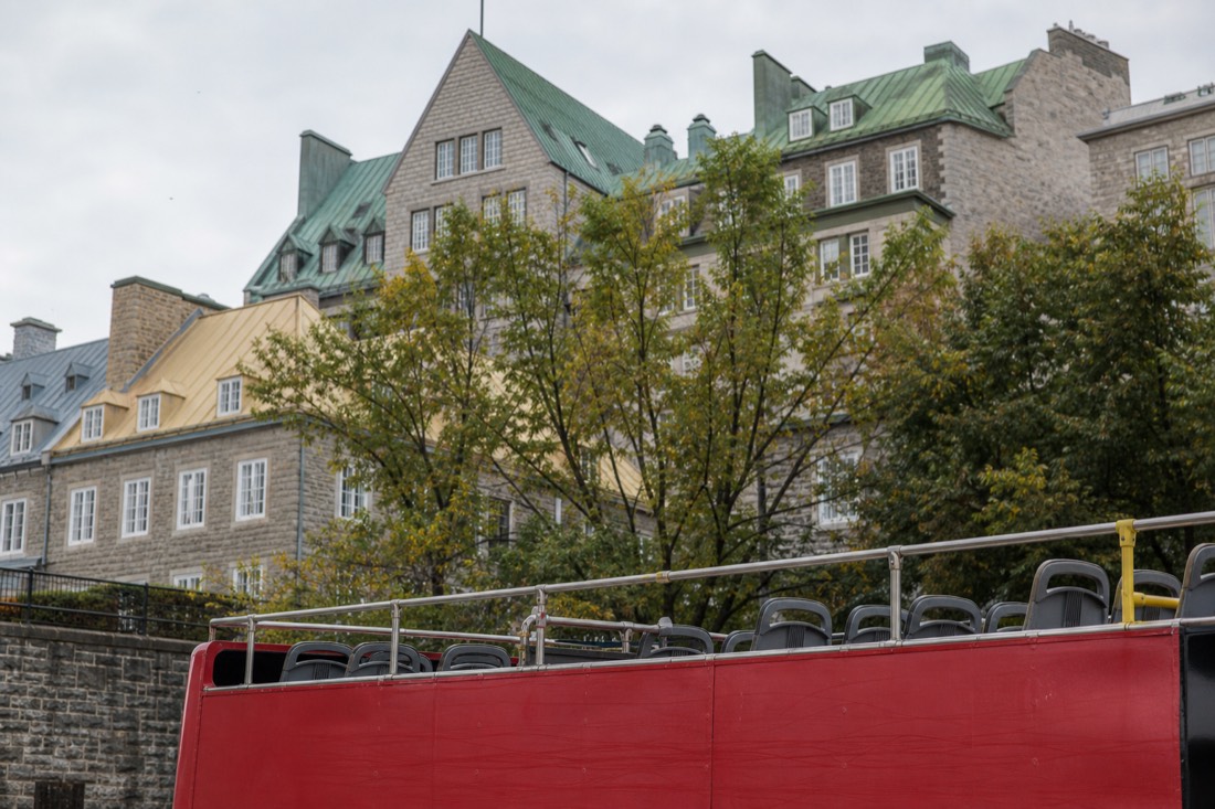An open-top double-decker sightseeing bus passing the old stone buildings of Quebec City